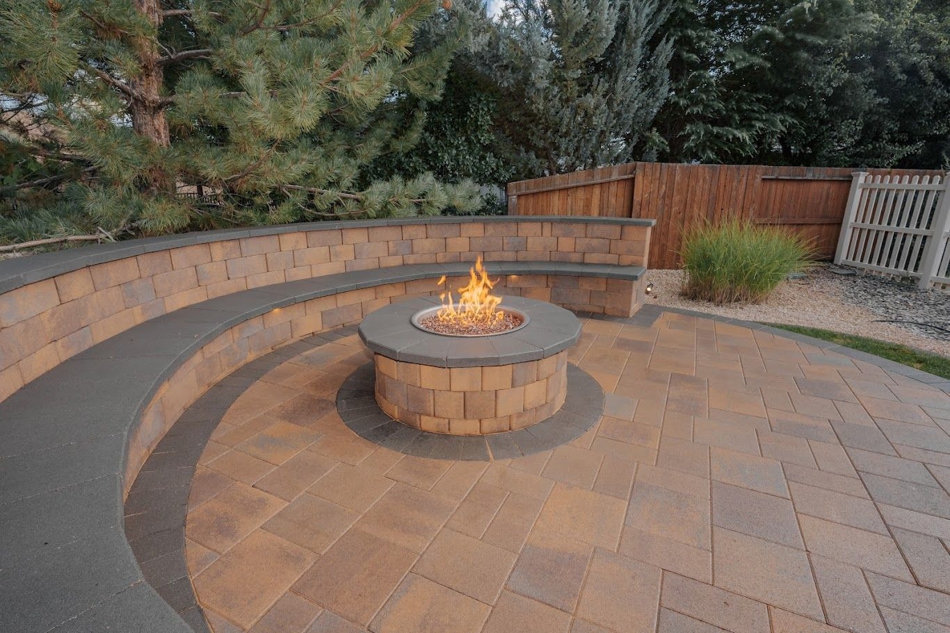Curved paver seat wall around a round gas fire pit on a paver patio