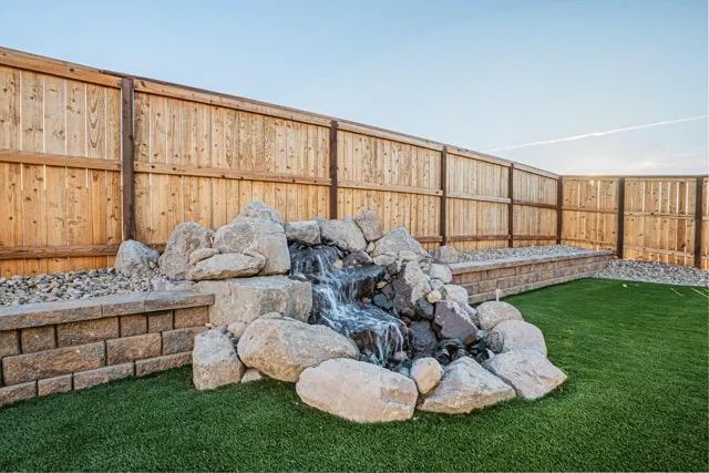 Boulder waterfall feature beside a block seat wall and turf lawn